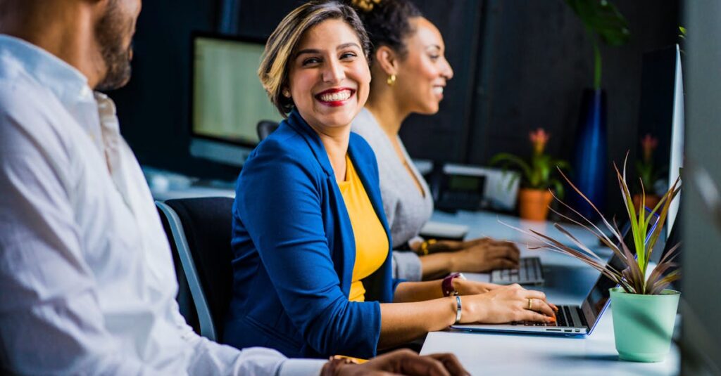 Three diverse professionals working and smiling at office desks, collaborating on generative engine optimisation strategies